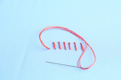 Sewing needle with thread and stitches on light blue cloth, above view