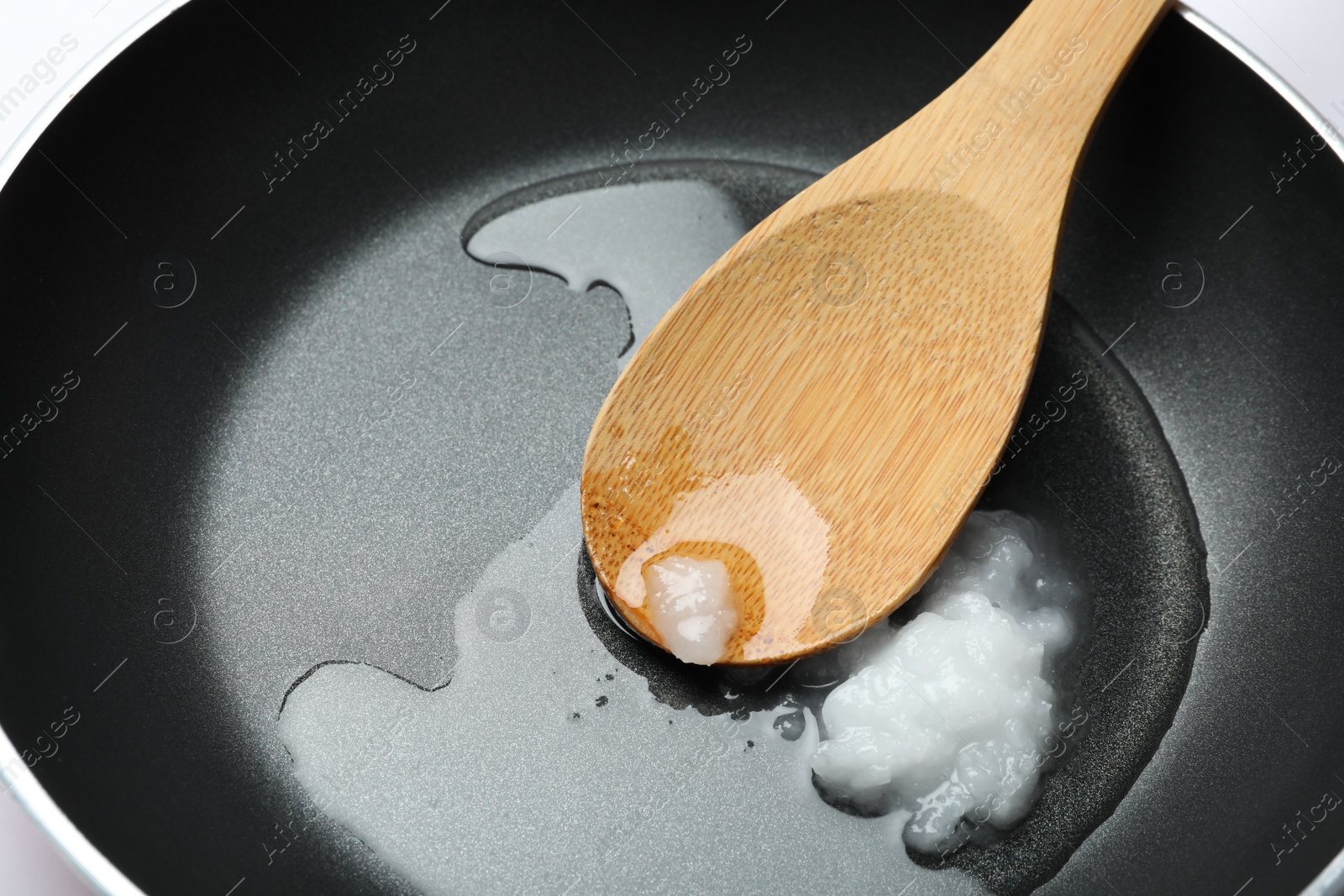 Photo of Frying pan with coconut oil and wooden spoon, closeup. Healthy cooking