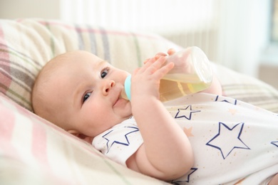 Pretty baby drinking from bottle on bed at home