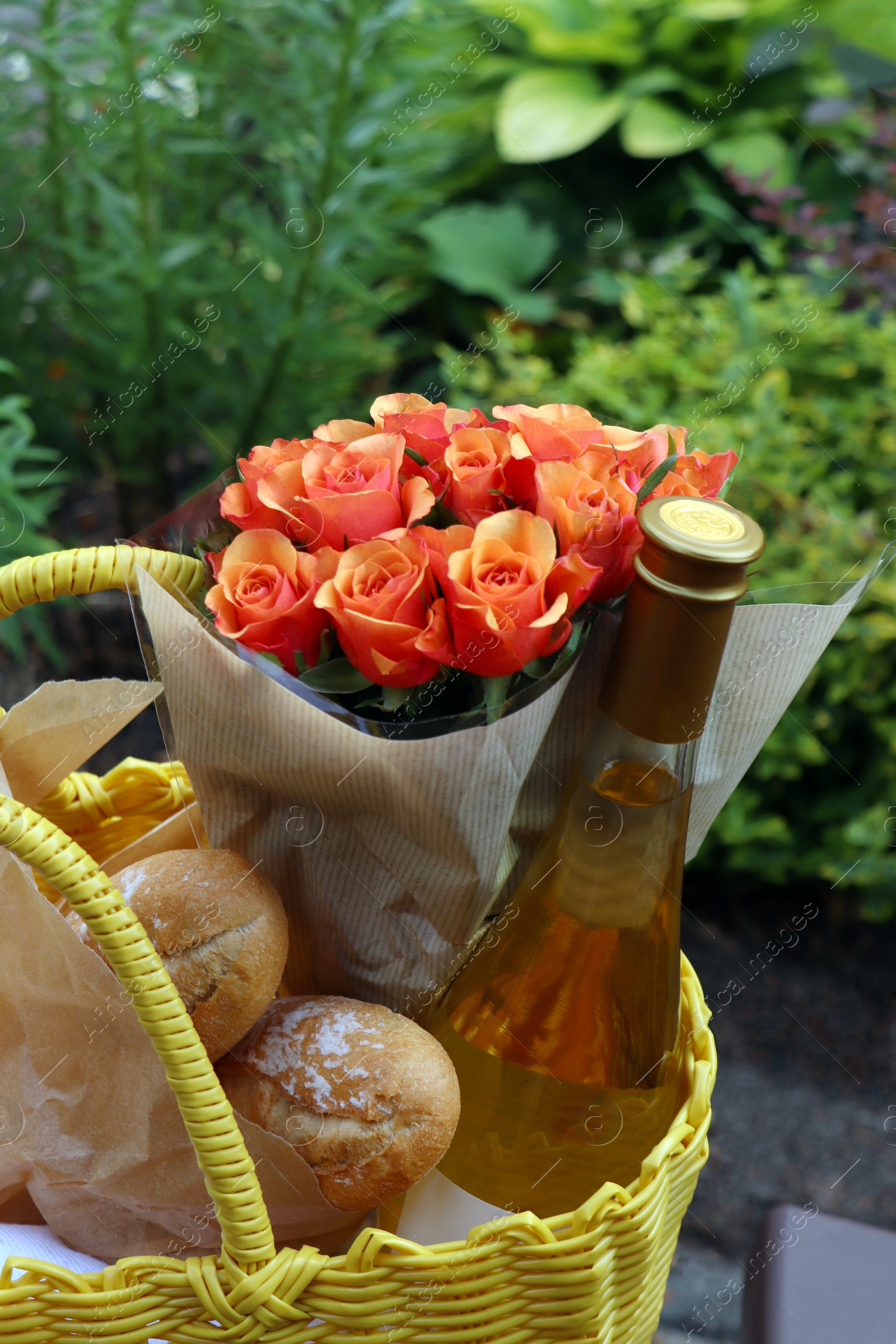 Photo of Yellow wicker bag with beautiful roses, bottle of wine and baguettes in garden