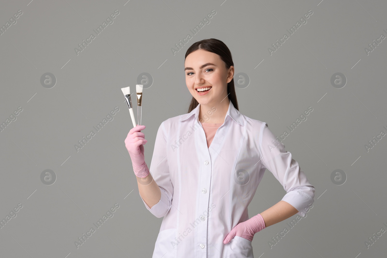 Photo of Cosmetologist with cosmetic brushes on grey background