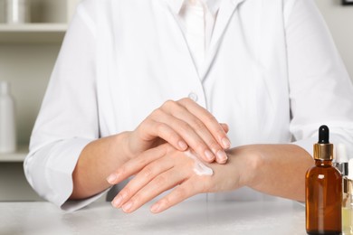 Photo of Dermatologist testing cosmetic product at white table indoors, closeup