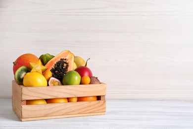 Photo of Different tropical fruits in box on white wooden table. Space for text