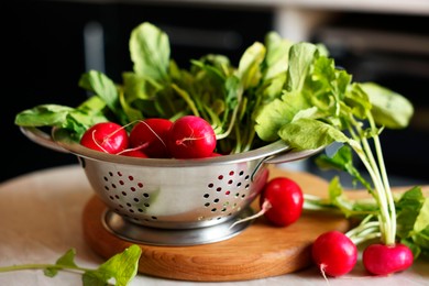 Metal colander with fresh radishes on white table, closeup