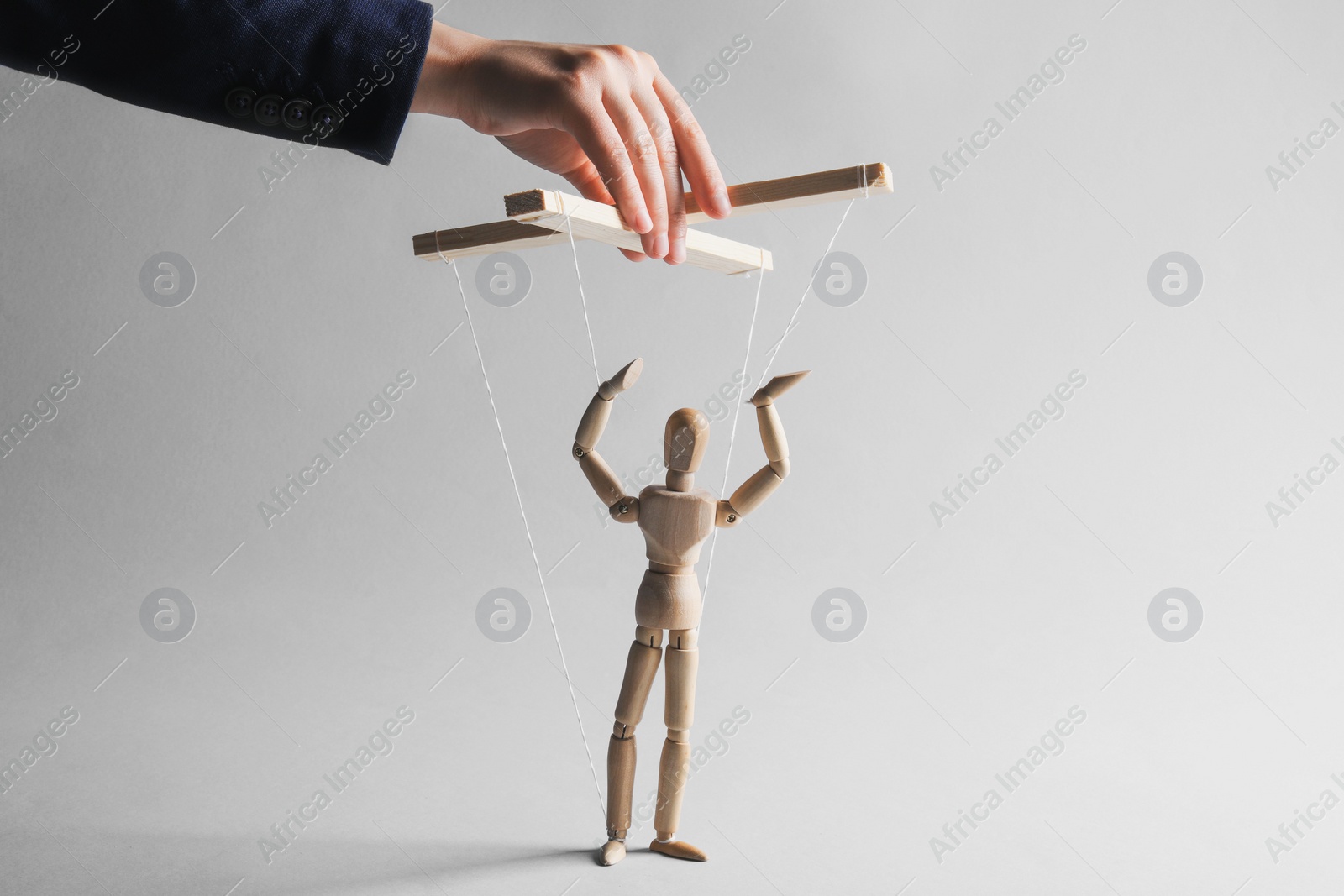 Photo of Woman pulling strings of puppet on light grey background, closeup