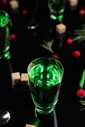 Absinthe in shot glass on mirror table, closeup. Alcoholic drink