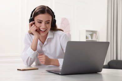 Happy woman with headphones using laptop at white table in room