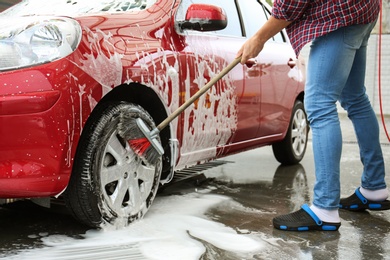 Young man cleaning vehicle with brush at self-service car wash