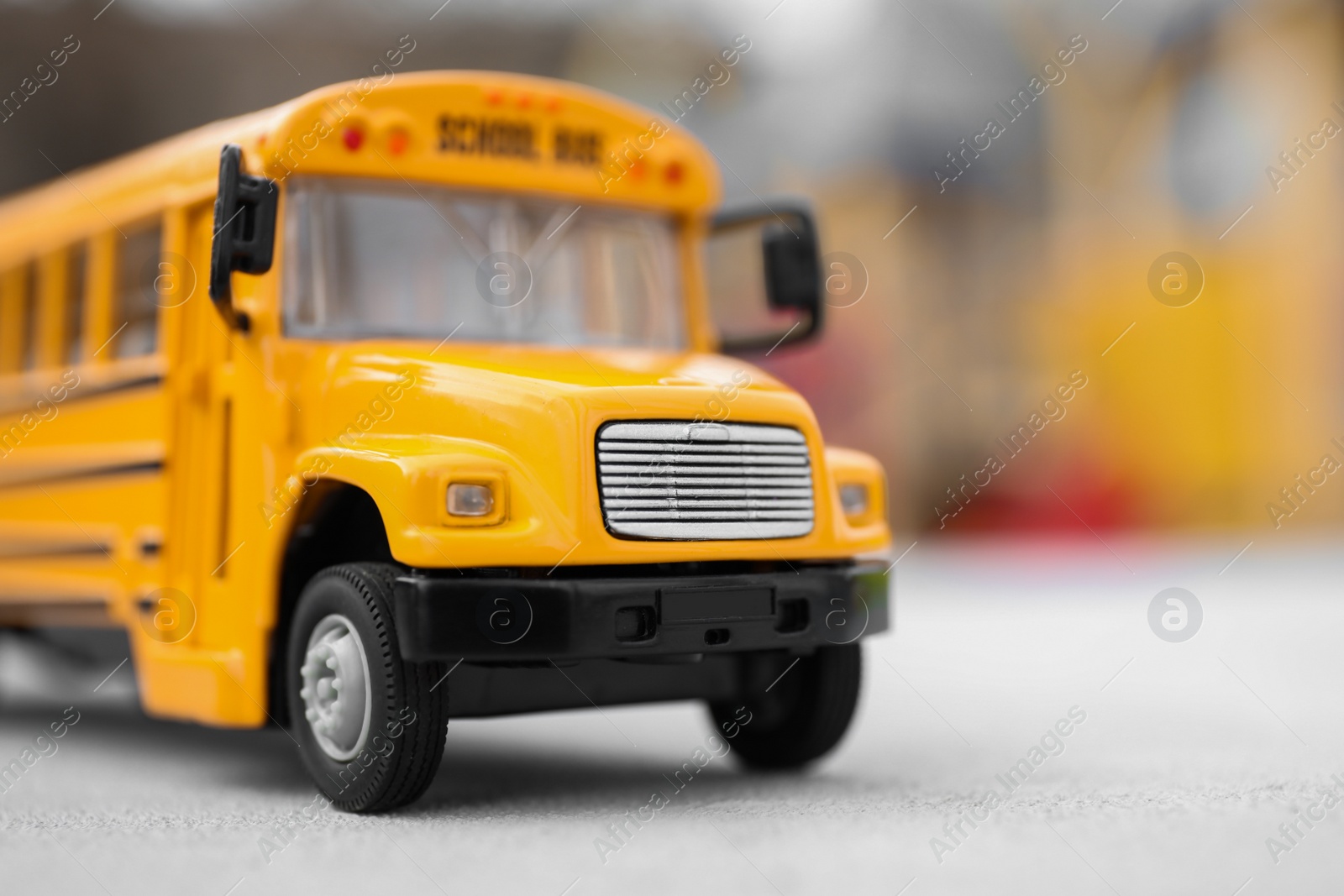 Photo of Yellow toy school bus against blurred 
background, closeup. Transport for students