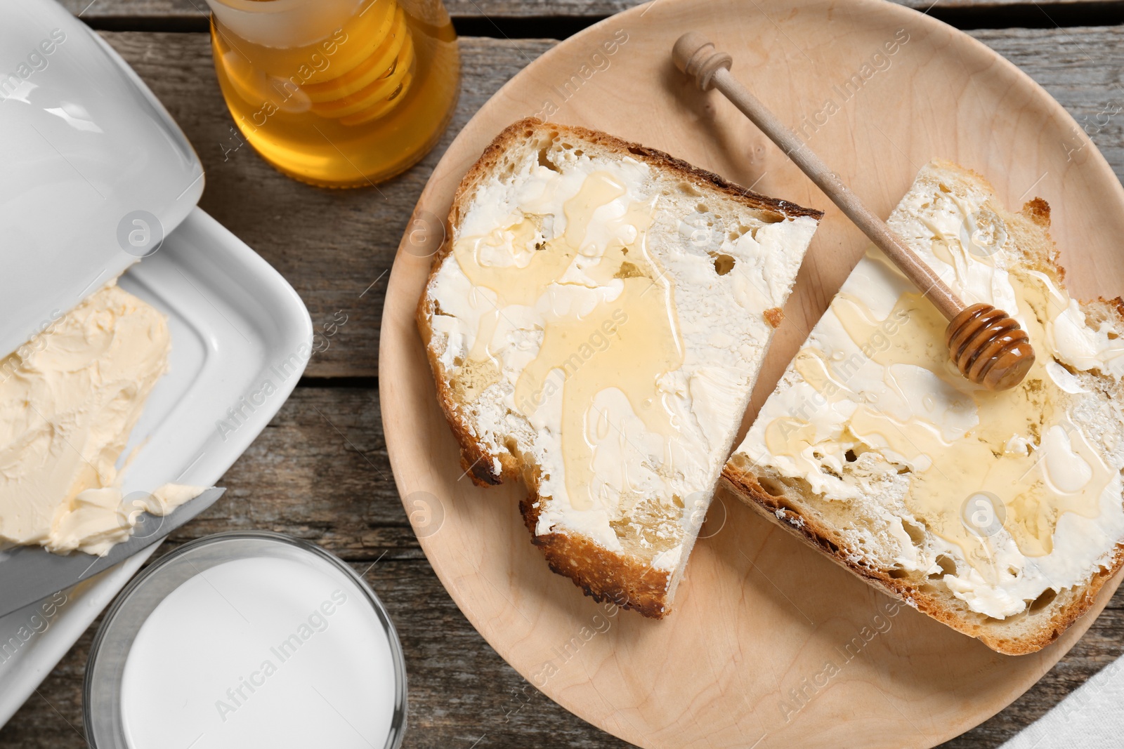 Photo of Slices of bread with butter, honey and milk on wooden table, flat lay