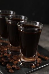 Photo of Shot glasses with coffee liqueur and beans on grey table, closeup
