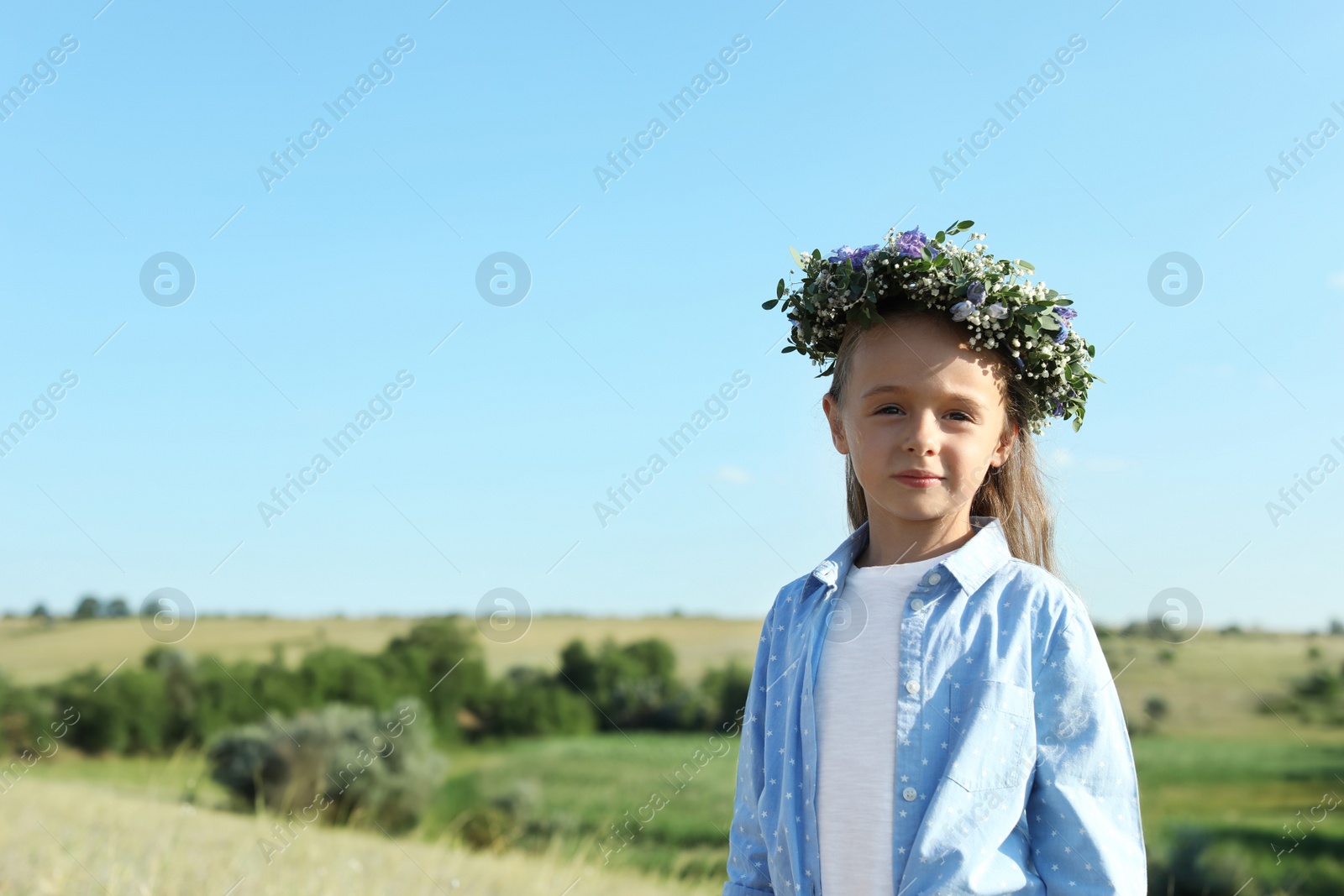 Photo of Cute little girl wearing flower wreath outdoors, space for text. Child spending time in nature