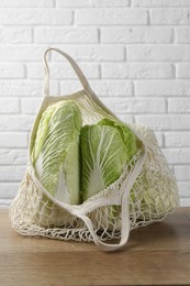 Fresh Chinese cabbages in string bag on wooden table near white brick wall