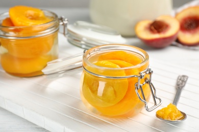 Glass jar with conserved peach halves on wooden board