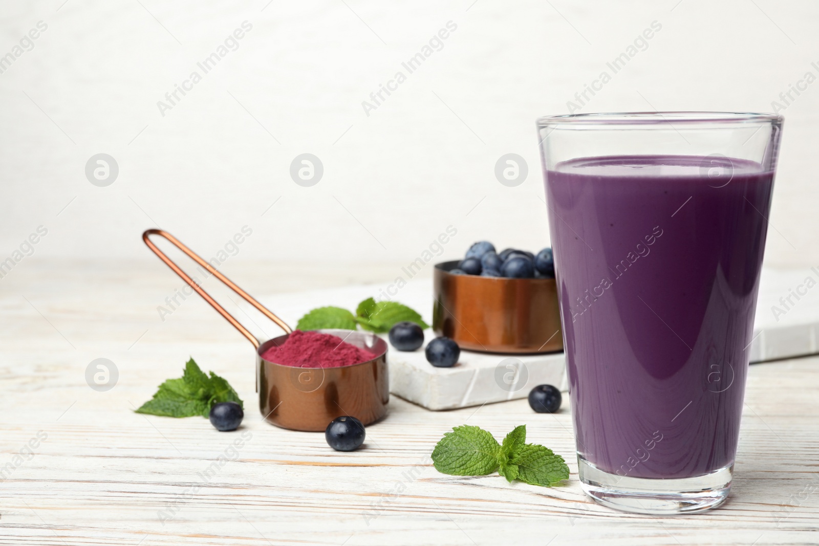 Photo of Tasty acai drink in glass, berries and powder on white wooden table