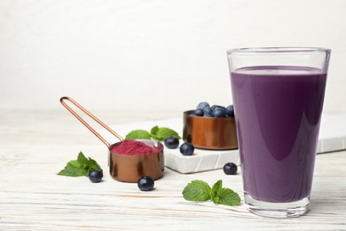 Tasty acai drink in glass, berries and powder on white wooden table