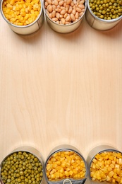 Photo of Open tin cans of conserved vegetables on wooden table, flat lay with space for text