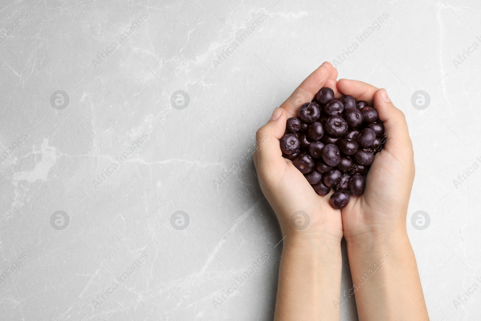 Photo of Top view of woman holding fresh acai berries on stone background, closeup. Space for text