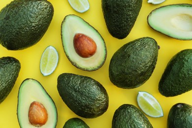 Photo of Many fresh whole and cut avocados with limes on yellow background, flat lay