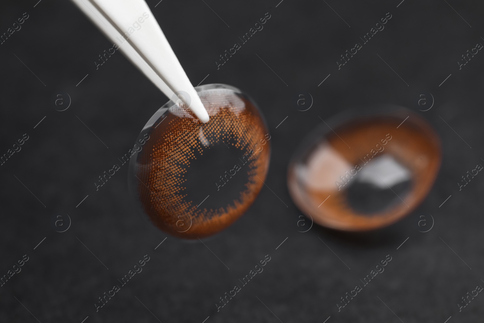 Photo of Tweezers with color contact lens on dark background, closeup. Space for text