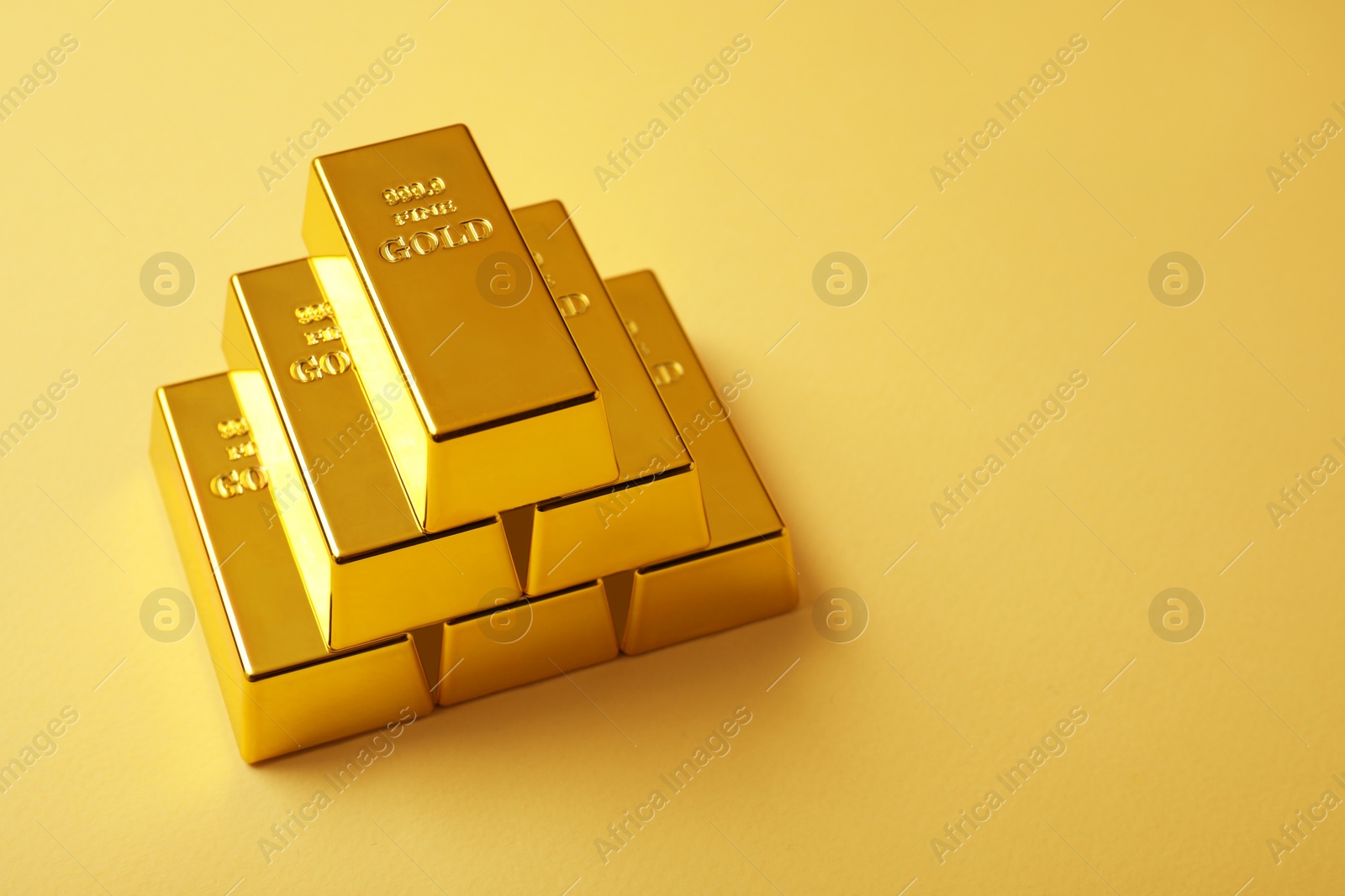 Photo of Stack of shiny gold bars on yellow background. Space for text