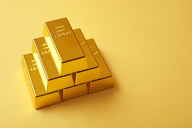 Stack of shiny gold bars on yellow background. Space for text