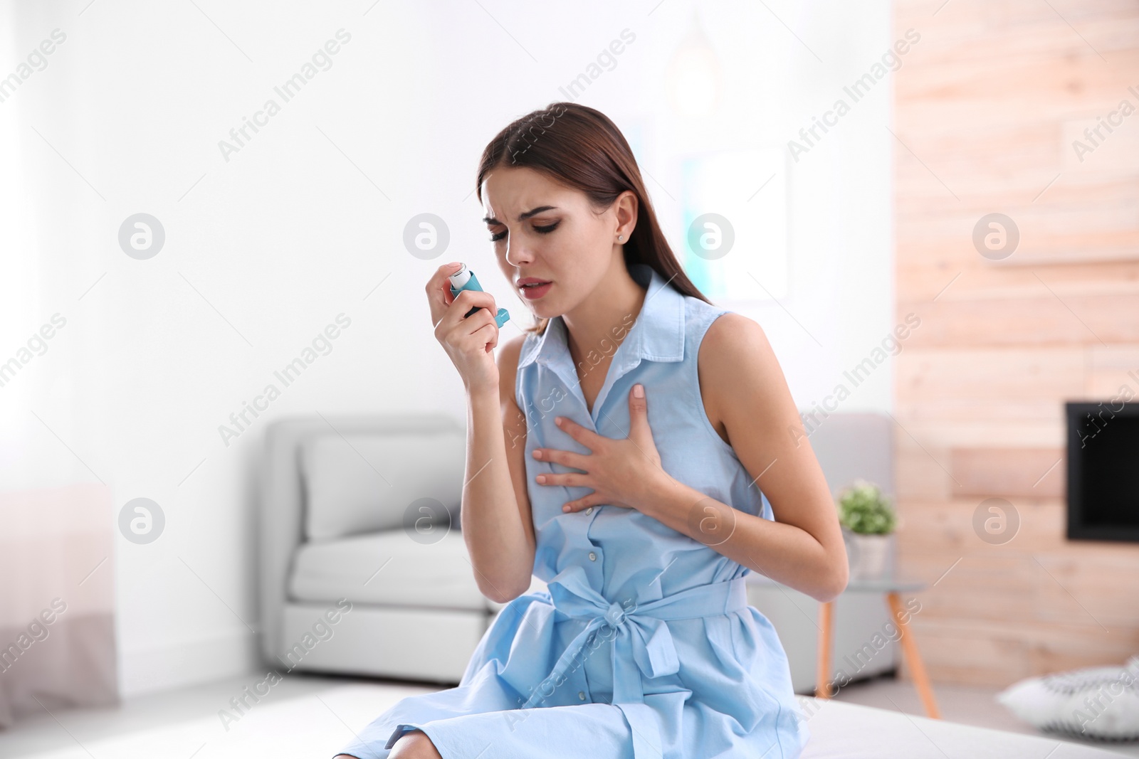 Photo of Young woman with asthma inhaler in light room