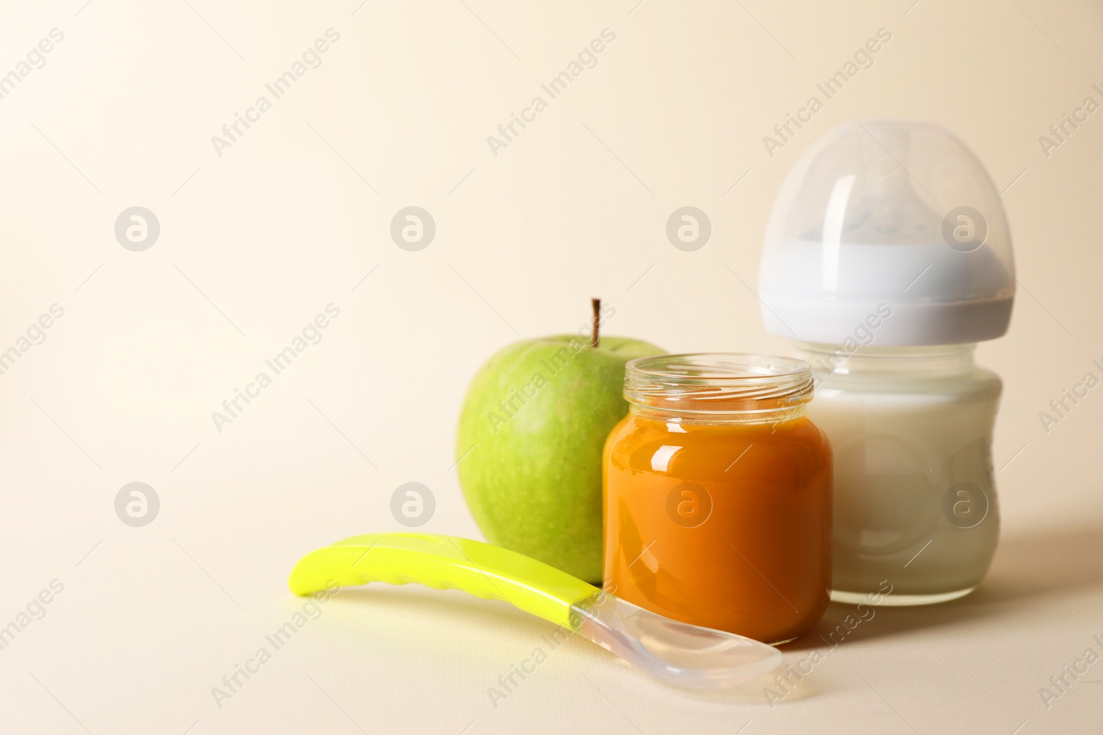 Photo of Healthy baby food in jar, bottle of milk, apple and spoon on beige background. Space for text