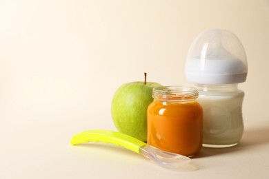 Photo of Healthy baby food in jar, bottle of milk, apple and spoon on beige background. Space for text