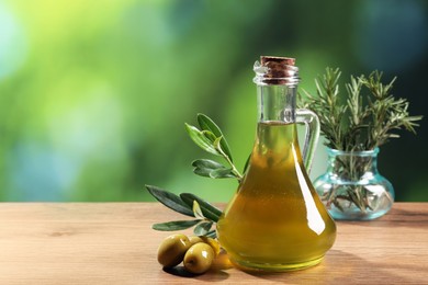 Photo of Jug of cooking oil, olives and green leaves on wooden table against blurred background. Space for text