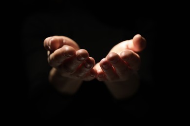 Photo of Religion. Woman with open palms praying on black background, closeup