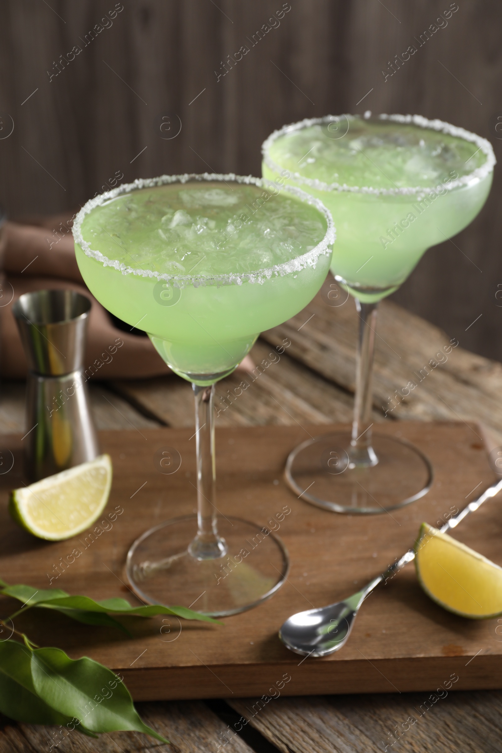 Photo of Delicious Margarita cocktail in glasses, lime and bar spoon on wooden table