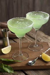 Delicious Margarita cocktail in glasses, lime and bar spoon on wooden table