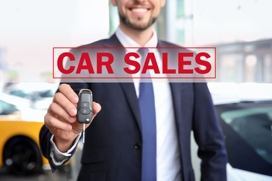 Salesman with key in car dealership, closeup