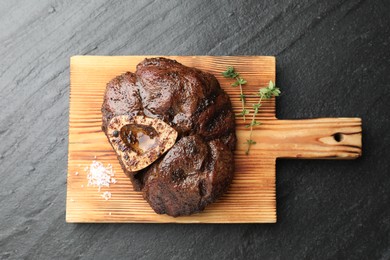 Photo of Piece of delicious grilled beef meat, thyme and salt on black table, top view