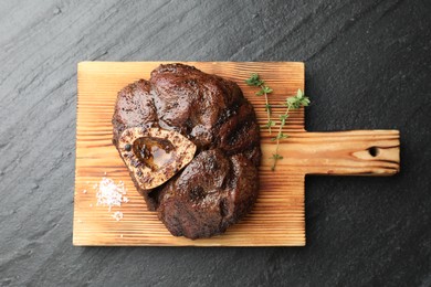 Piece of delicious grilled beef meat, thyme and salt on black table, top view