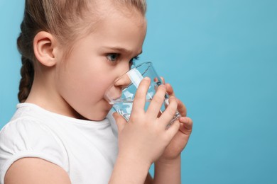 Photo of Cute little girl drinking fresh water from glass on light blue background, space for text