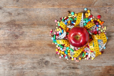 Weight loss pills with apple and measuring tape on wooden background, top view. Space for text