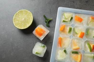 Photo of Ice cube tray with frozen fruits and mint on grey table, flat lay