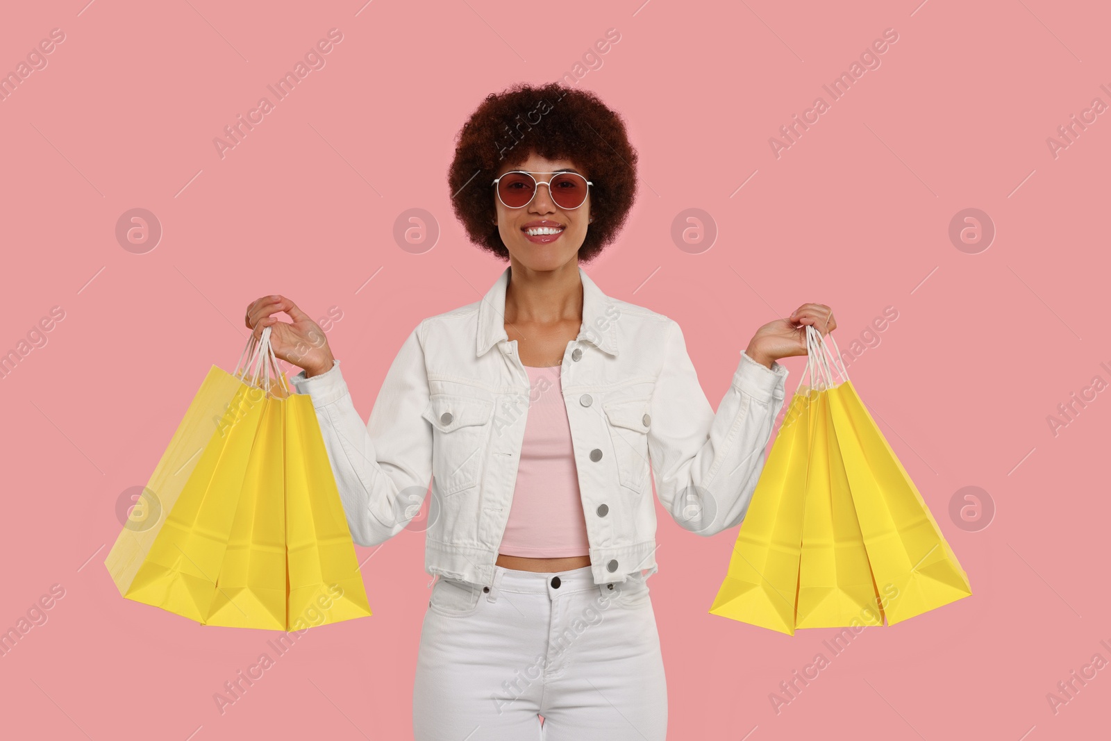 Photo of Happy young woman in stylish sunglasses with shopping bags on pink background