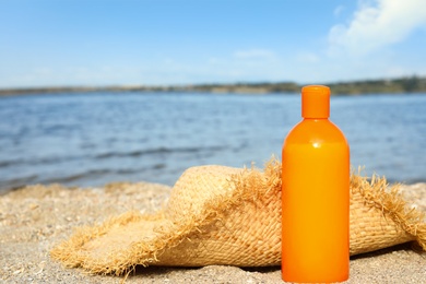 Photo of Bottle of sun protection body cream and hat on beach, space for design