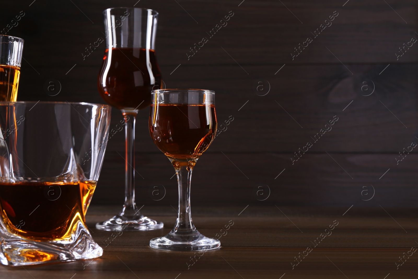 Photo of Different delicious liqueurs in glasses on wooden table. Space for text