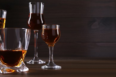 Different delicious liqueurs in glasses on wooden table. Space for text