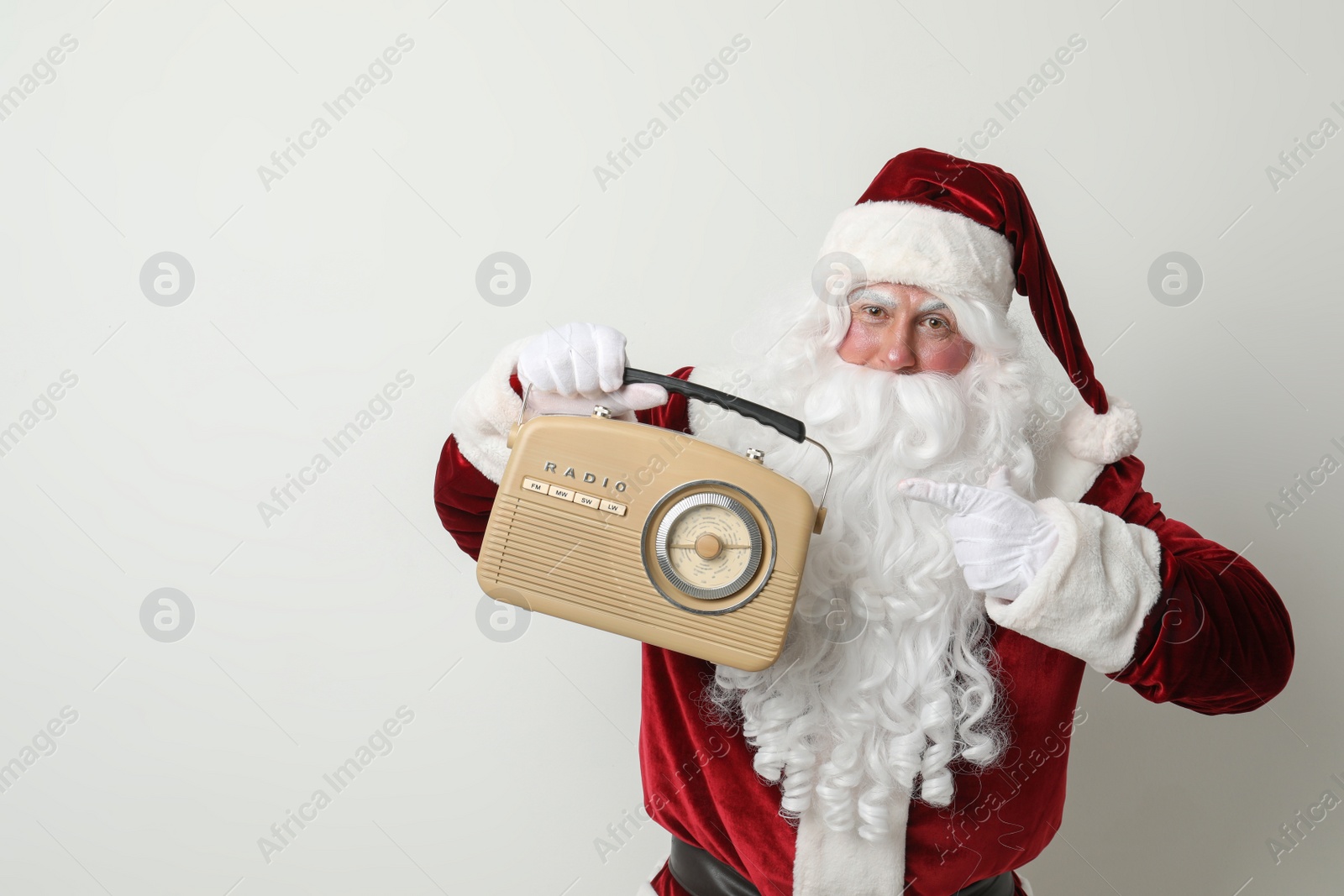 Photo of Santa Claus with vintage radio on light background, space for text. Christmas music