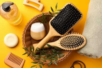 Photo of Wooden brushes and different hair products on orange background, above view