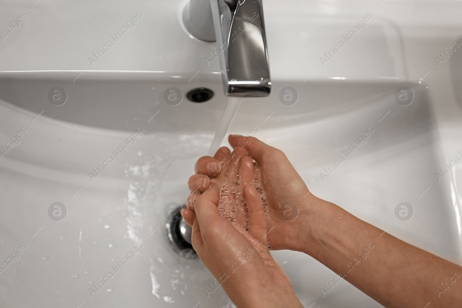 Photo of Woman washing hands under tap indoors, closeup