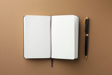Photo of Open notebook with blank pages and pen on light brown background, top view. Space for text