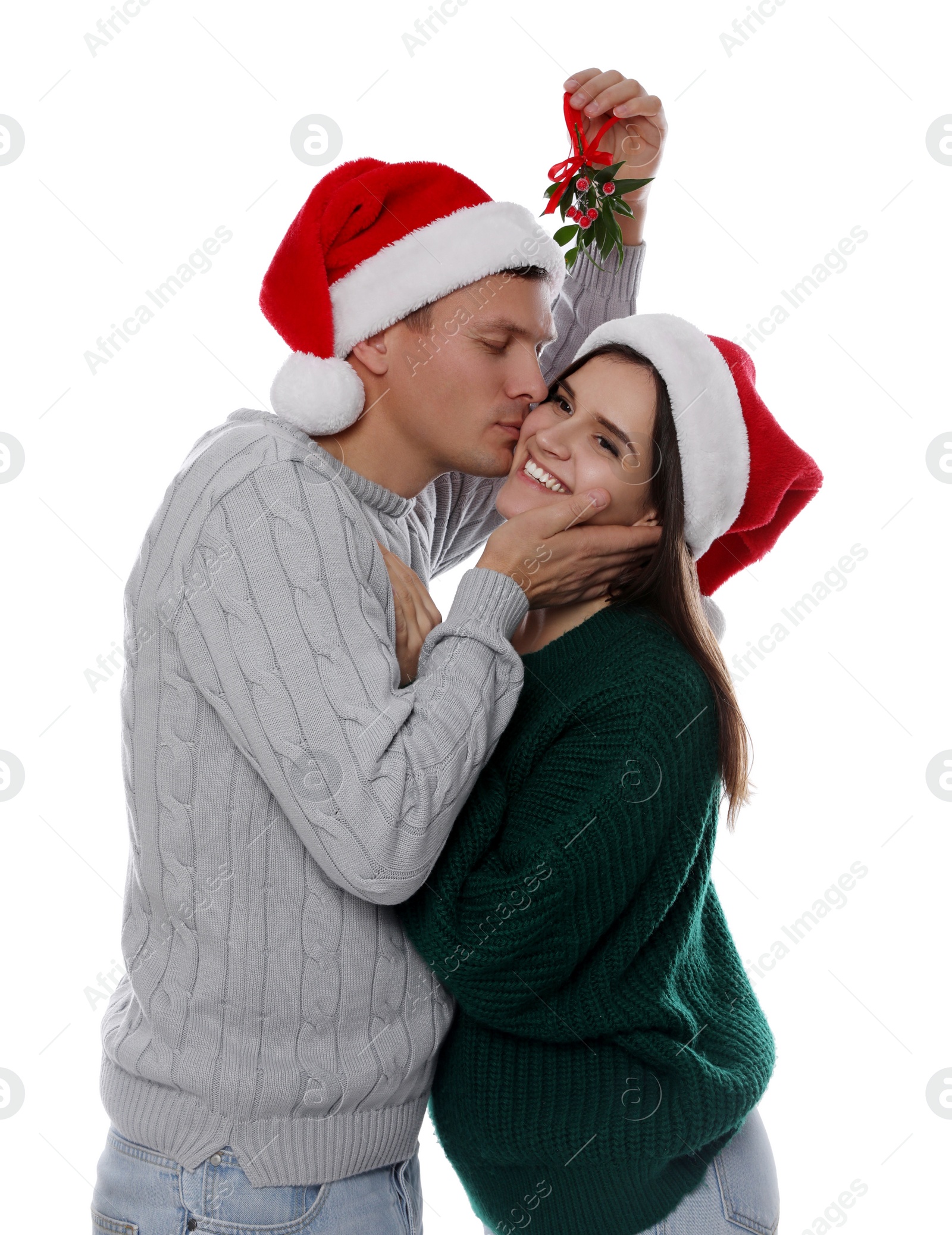 Photo of Happy man kissing his girlfriend under mistletoe bunch on white background