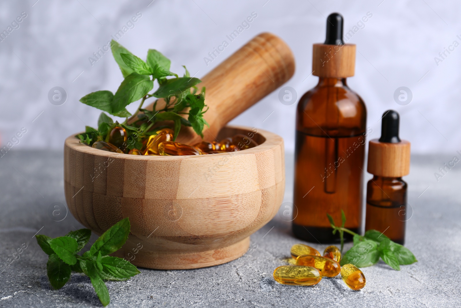 Photo of Wooden mortar with fresh green herbs, extracts and capsules on light grey table