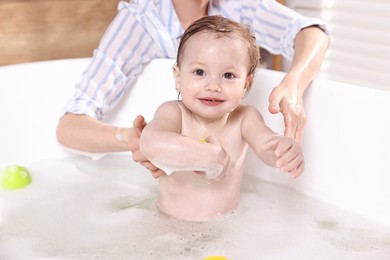 Mother bathing her cute little baby in tub at home